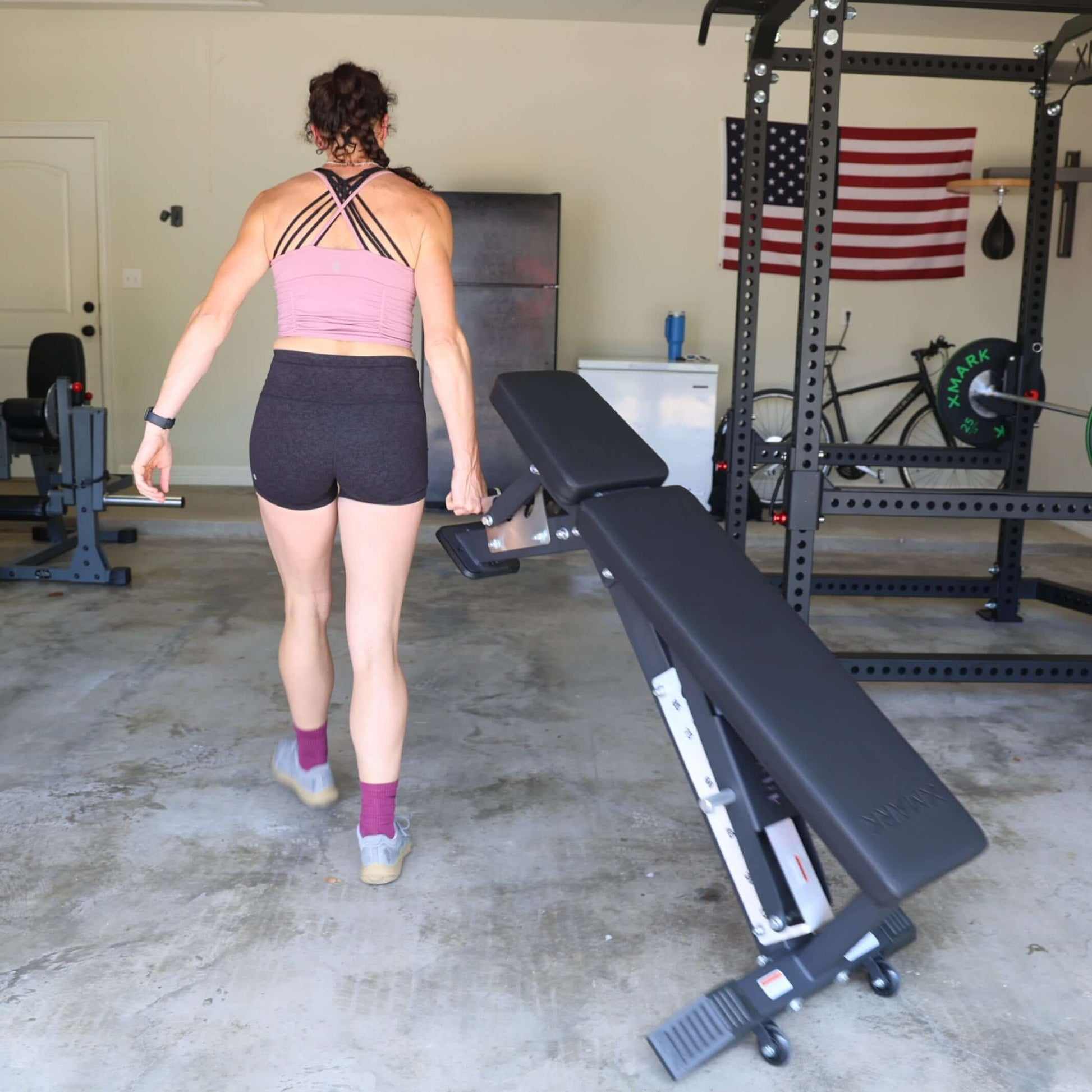 A person carrying a Black Hawk Commercial Adjustable Weight Bench in a garage gym, showcasing its portable design.
