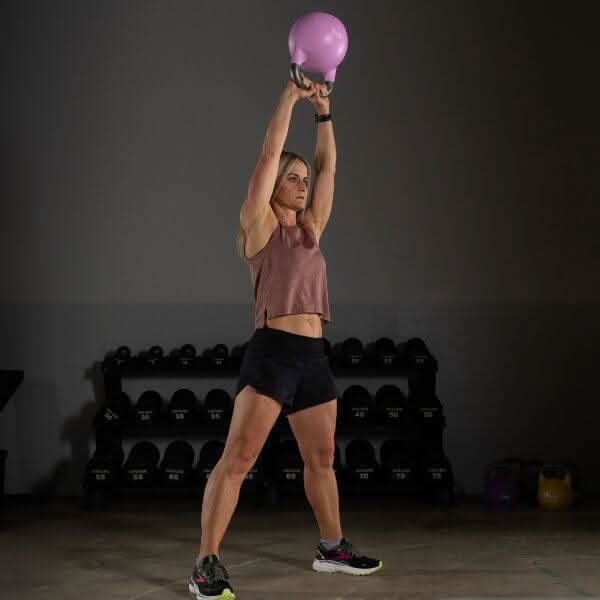 Woman lifting a pink kettlebell overhead in a gym, showcasing competition kettlebells for fitness enthusiasts.