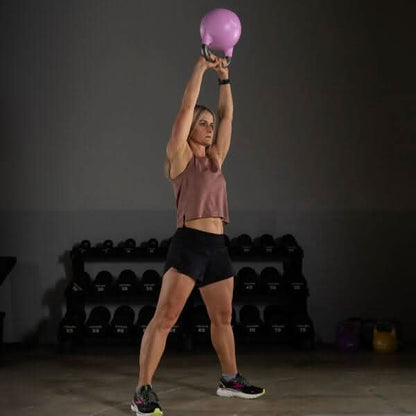 Woman lifting a pink kettlebell overhead in a gym, showcasing competition kettlebells for fitness enthusiasts.