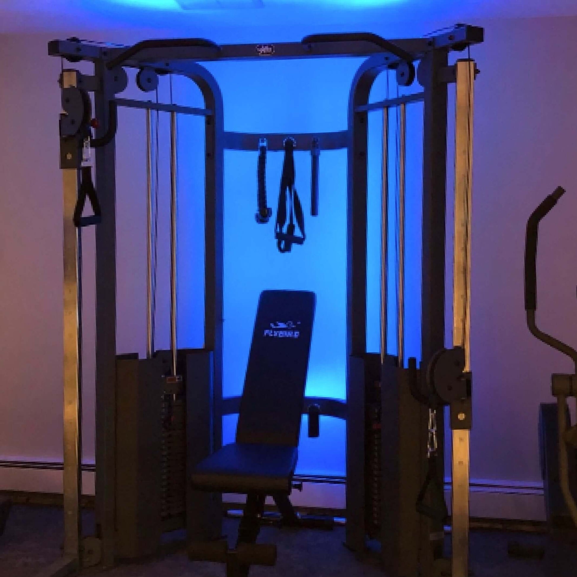 Functional trainer cable machine with adjustable weight bench and blue ambient lighting, perfect for versatile workouts.