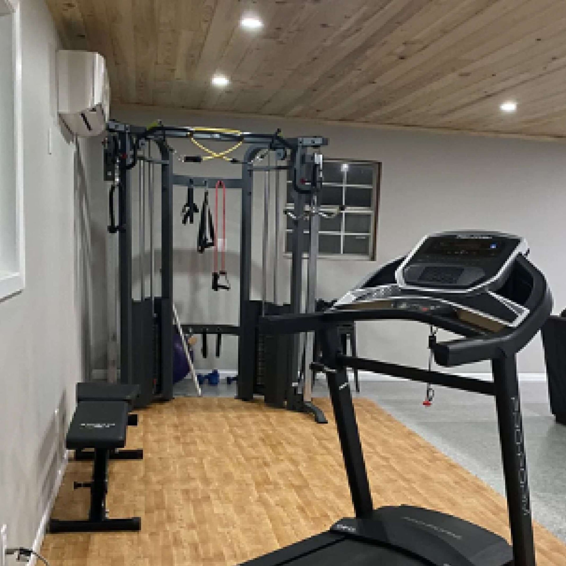 Home gym setup featuring a functional trainer cable machine and treadmill on a hardwood floor.